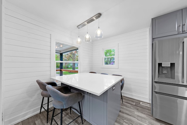 kitchen featuring gray cabinets, a kitchen breakfast bar, stainless steel refrigerator with ice dispenser, and wood finished floors