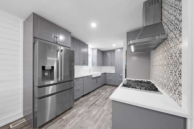 kitchen featuring light wood-type flooring, gas cooktop, wall chimney exhaust hood, gray cabinetry, and stainless steel fridge with ice dispenser