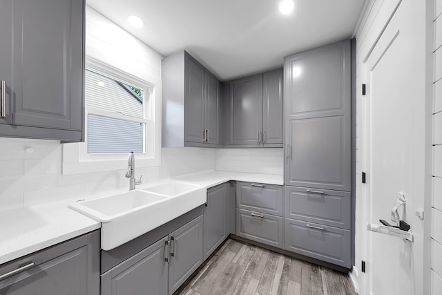 kitchen featuring light wood finished floors, gray cabinets, tasteful backsplash, and a sink