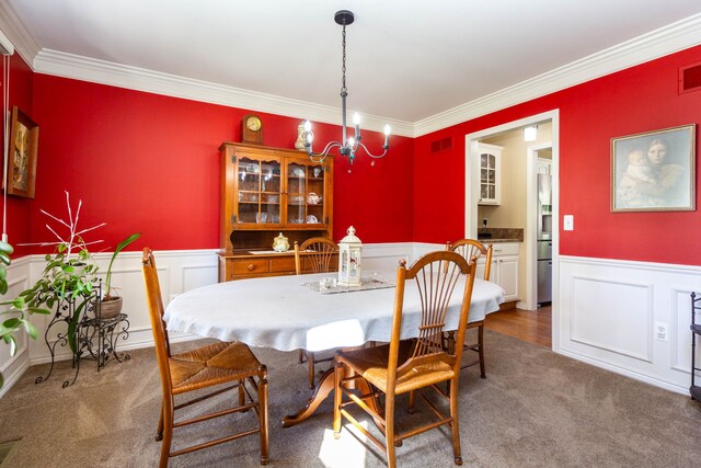 carpeted dining space featuring visible vents, ornamental molding, wainscoting, and a chandelier