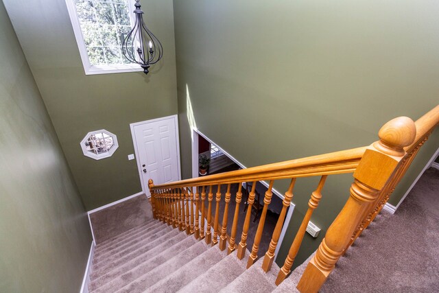stairs featuring carpet flooring, baseboards, a notable chandelier, and a high ceiling