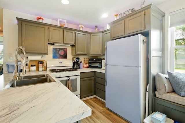 kitchen featuring white appliances, light wood-style floors, light countertops, a sink, and backsplash