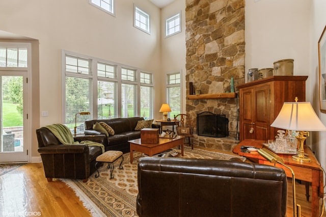 living area featuring a stone fireplace, light wood finished floors, and a towering ceiling