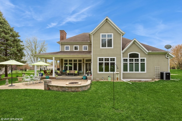 back of house with a chimney, roof with shingles, a patio area, central air condition unit, and an outdoor living space with a fire pit