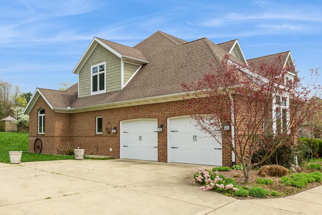 view of side of property featuring a garage, a shingled roof, concrete driveway, and brick siding