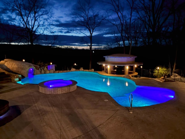 pool at twilight with a pool with connected hot tub, fence, and a patio area