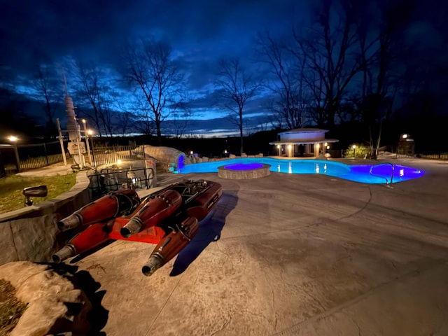 pool at night featuring fence, a patio, and an outdoor pool