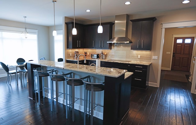 kitchen with backsplash, dark wood-style floors, black electric stovetop, a breakfast bar, and wall chimney exhaust hood