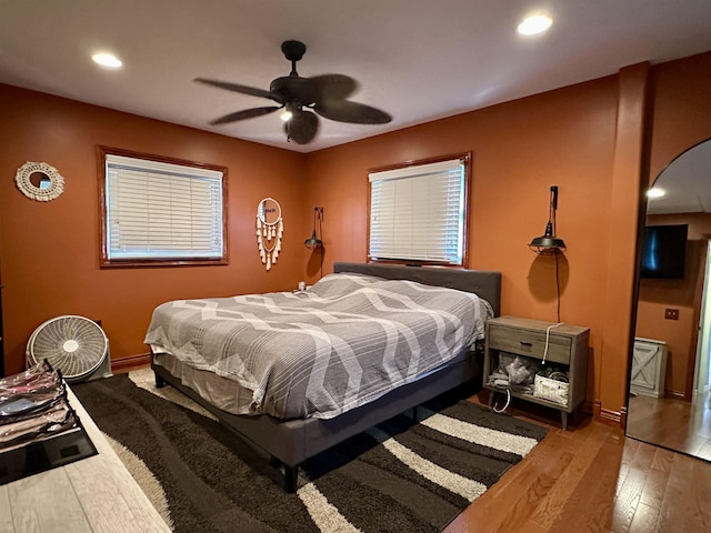 bedroom featuring a ceiling fan, arched walkways, wood finished floors, baseboards, and recessed lighting