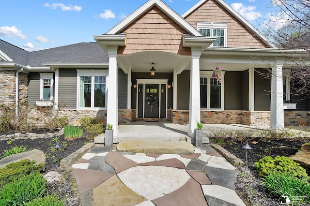 doorway to property featuring covered porch, a shingled roof, and stone siding