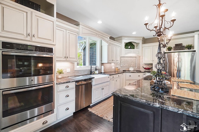 kitchen with a sink, dark stone counters, dark wood finished floors, and stainless steel appliances