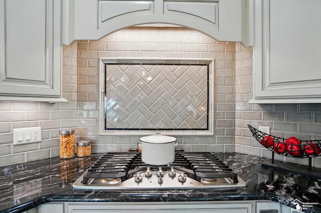 room details featuring stainless steel gas stovetop, backsplash, dark stone countertops, and white cabinetry