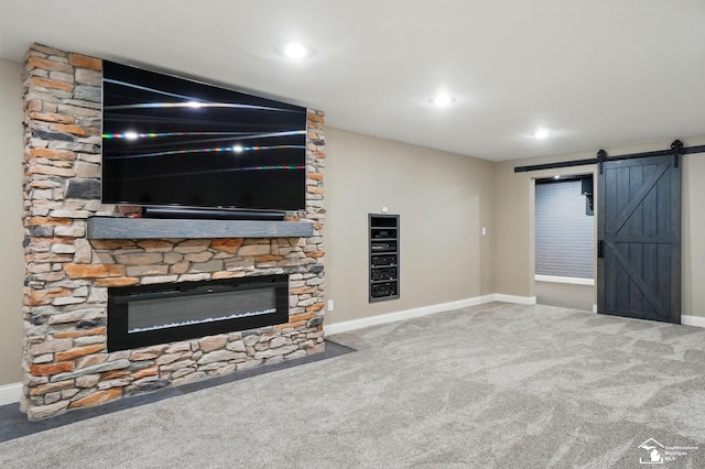 unfurnished living room featuring baseboards, a barn door, and carpet