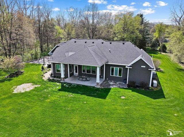 back of house featuring a lawn, roof with shingles, and a patio area