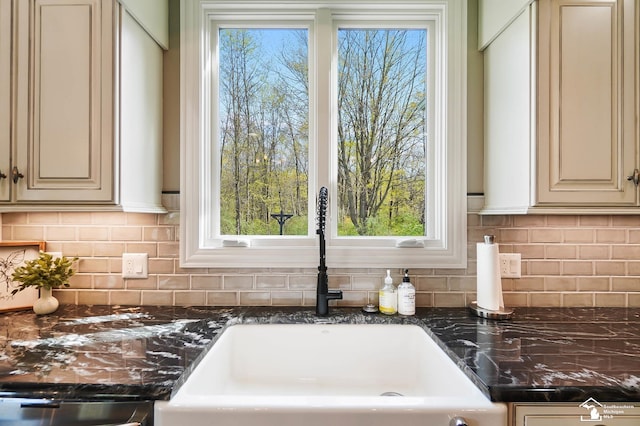 interior details featuring cream cabinets, decorative backsplash, a sink, and dark stone countertops