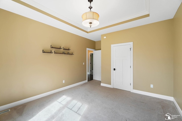 unfurnished bedroom featuring carpet floors, baseboards, a tray ceiling, and visible vents
