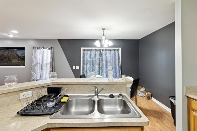 kitchen featuring baseboards, light wood-type flooring, light countertops, a sink, and a notable chandelier