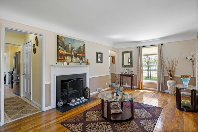 living area featuring visible vents, a fireplace with flush hearth, baseboards, and hardwood / wood-style floors