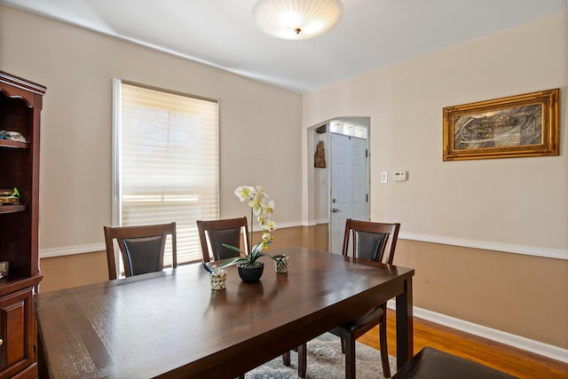 dining room with arched walkways, baseboards, and wood finished floors