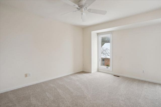 empty room with baseboards, ceiling fan, carpet flooring, and visible vents
