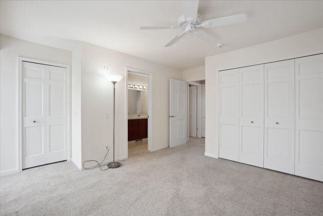 unfurnished bedroom with baseboards, light carpet, ceiling fan, and ensuite bathroom