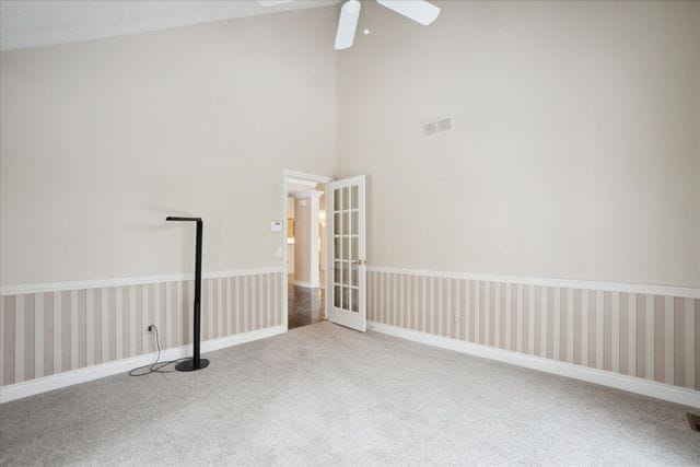 spare room with a high ceiling, french doors, carpet, a ceiling fan, and visible vents