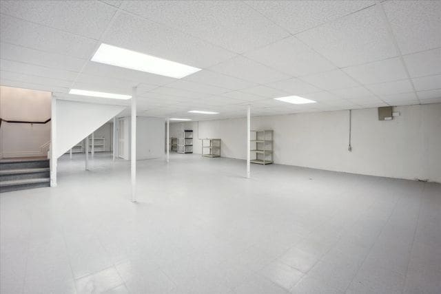 finished below grade area with a drop ceiling and stairway