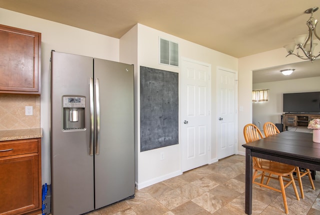 kitchen featuring brown cabinets, an inviting chandelier, stainless steel fridge, decorative backsplash, and visible vents