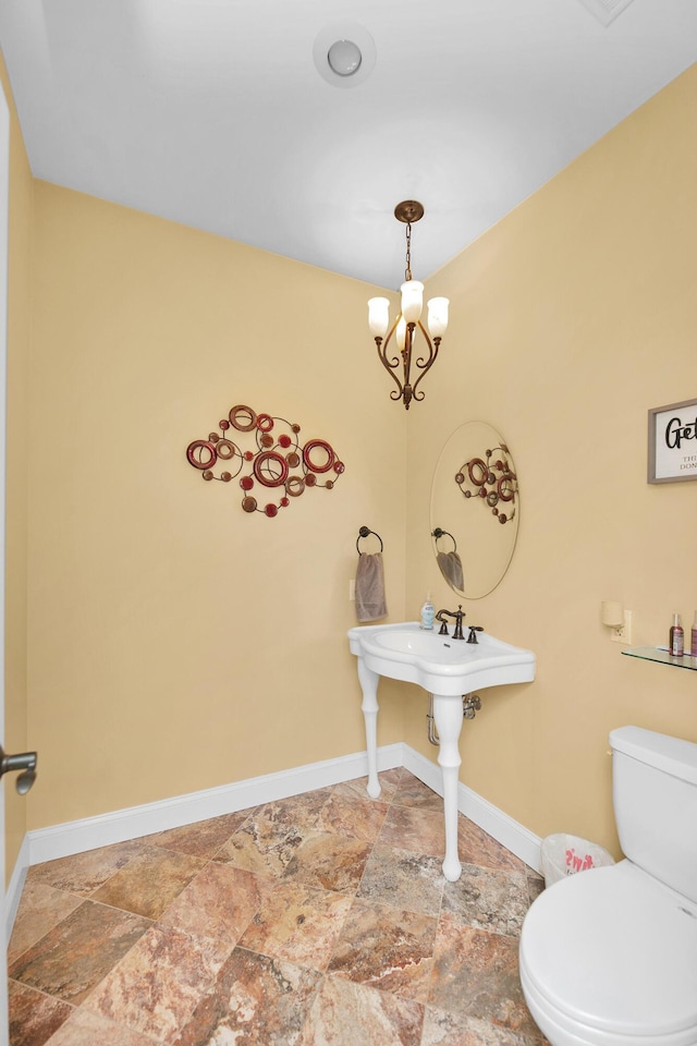 bathroom with baseboards, toilet, stone tile flooring, and a chandelier