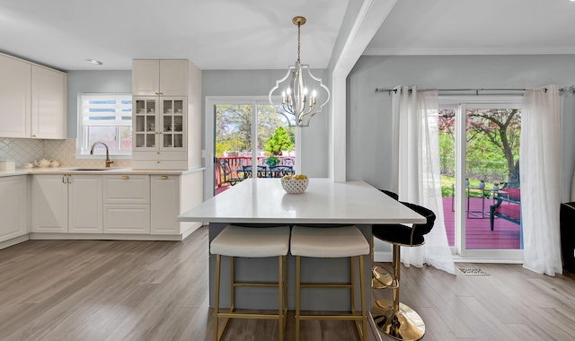 interior space with a breakfast bar area, a sink, light countertops, light wood finished floors, and a notable chandelier
