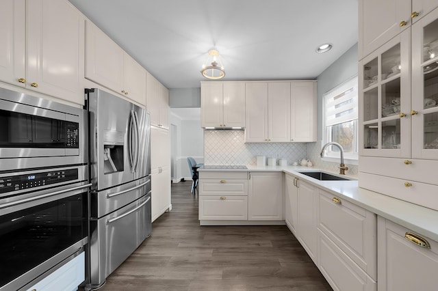 kitchen with appliances with stainless steel finishes, a sink, light countertops, white cabinetry, and decorative backsplash