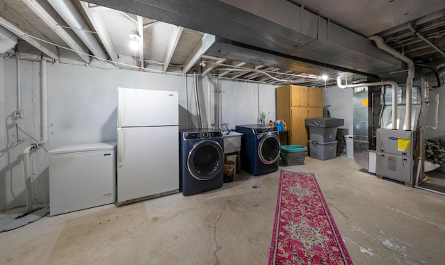 unfinished below grade area featuring freestanding refrigerator, heating unit, washer and dryer, and white fridge
