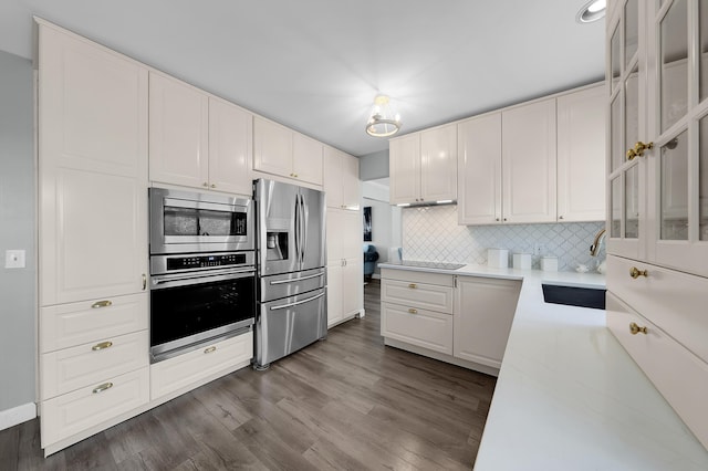 kitchen with appliances with stainless steel finishes, glass insert cabinets, a sink, and tasteful backsplash