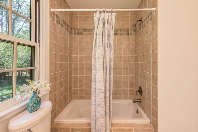 bathroom with tiled shower / bath, toilet, and a wealth of natural light