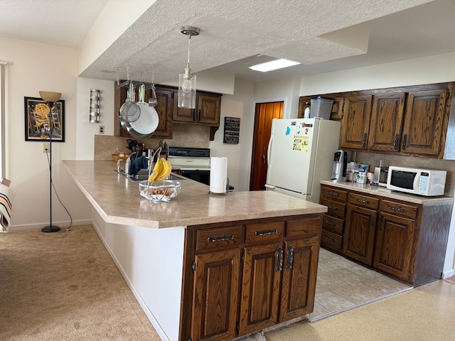 kitchen with a peninsula, dark brown cabinets, white appliances, light countertops, and backsplash