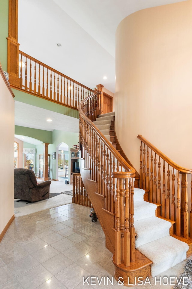 staircase with baseboards, a high ceiling, ornate columns, recessed lighting, and arched walkways