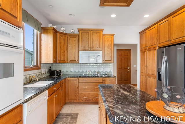 kitchen featuring brown cabinetry, a sink, backsplash, and white appliances