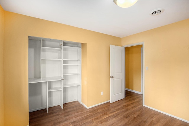 unfurnished bedroom with baseboards, visible vents, wood finished floors, and a closet