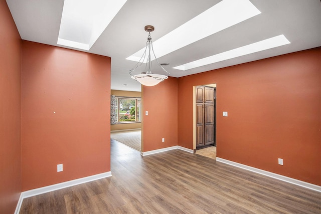 empty room with a skylight, baseboards, and wood finished floors