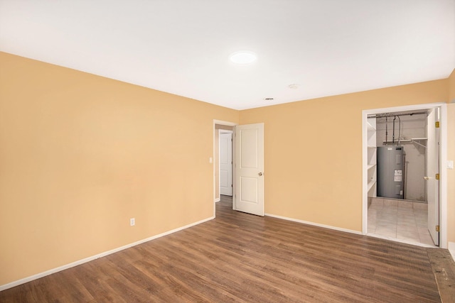 unfurnished bedroom with baseboards, wood finished floors, and electric water heater