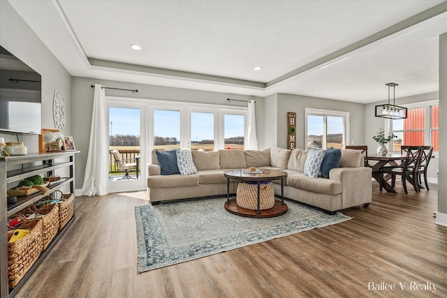 living area featuring baseboards, a notable chandelier, wood finished floors, and a tray ceiling