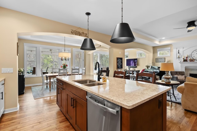 kitchen with a sink, a raised ceiling, dishwasher, light wood-style flooring, and open floor plan