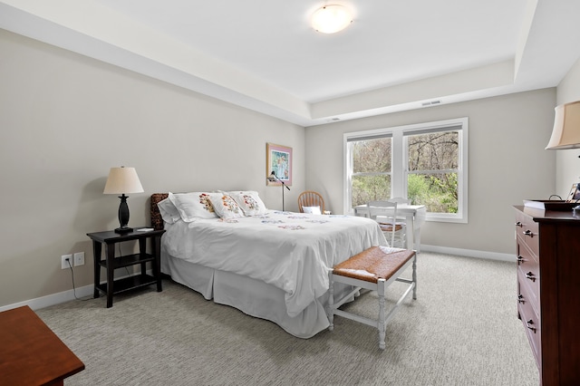 bedroom with visible vents, baseboards, light colored carpet, and a raised ceiling