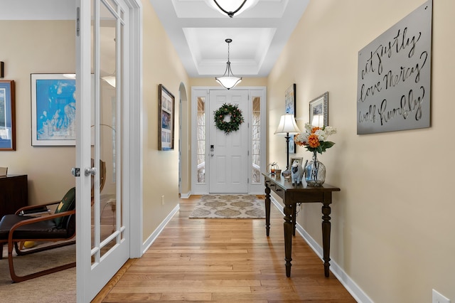 entrance foyer with light wood finished floors, french doors, baseboards, a tray ceiling, and ornamental molding