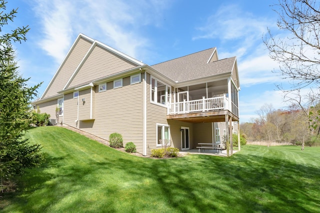 back of property featuring a yard, a patio, a shingled roof, and a sunroom