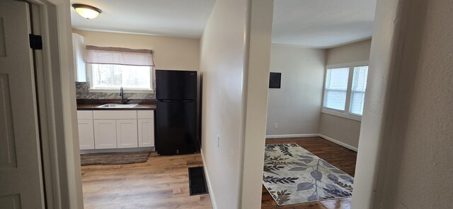 kitchen featuring white cabinets, dark countertops, a sink, light wood-style flooring, and freestanding refrigerator