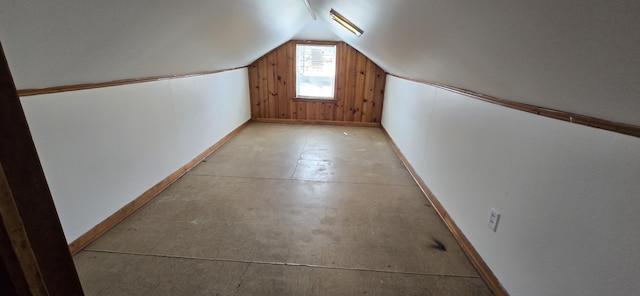 bonus room with baseboards, wood walls, concrete floors, and lofted ceiling