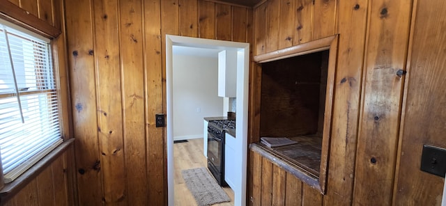 kitchen featuring brown cabinetry, wood walls, baseboards, black gas range oven, and light wood-style flooring