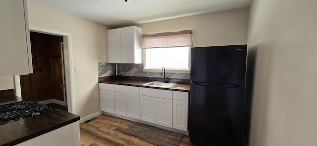 kitchen with decorative backsplash, wood finished floors, a sink, freestanding refrigerator, and white cabinetry
