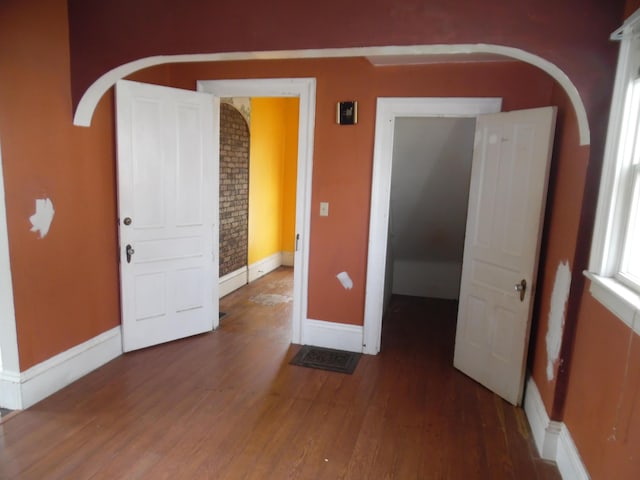 unfurnished room featuring arched walkways, baseboards, and wood finished floors